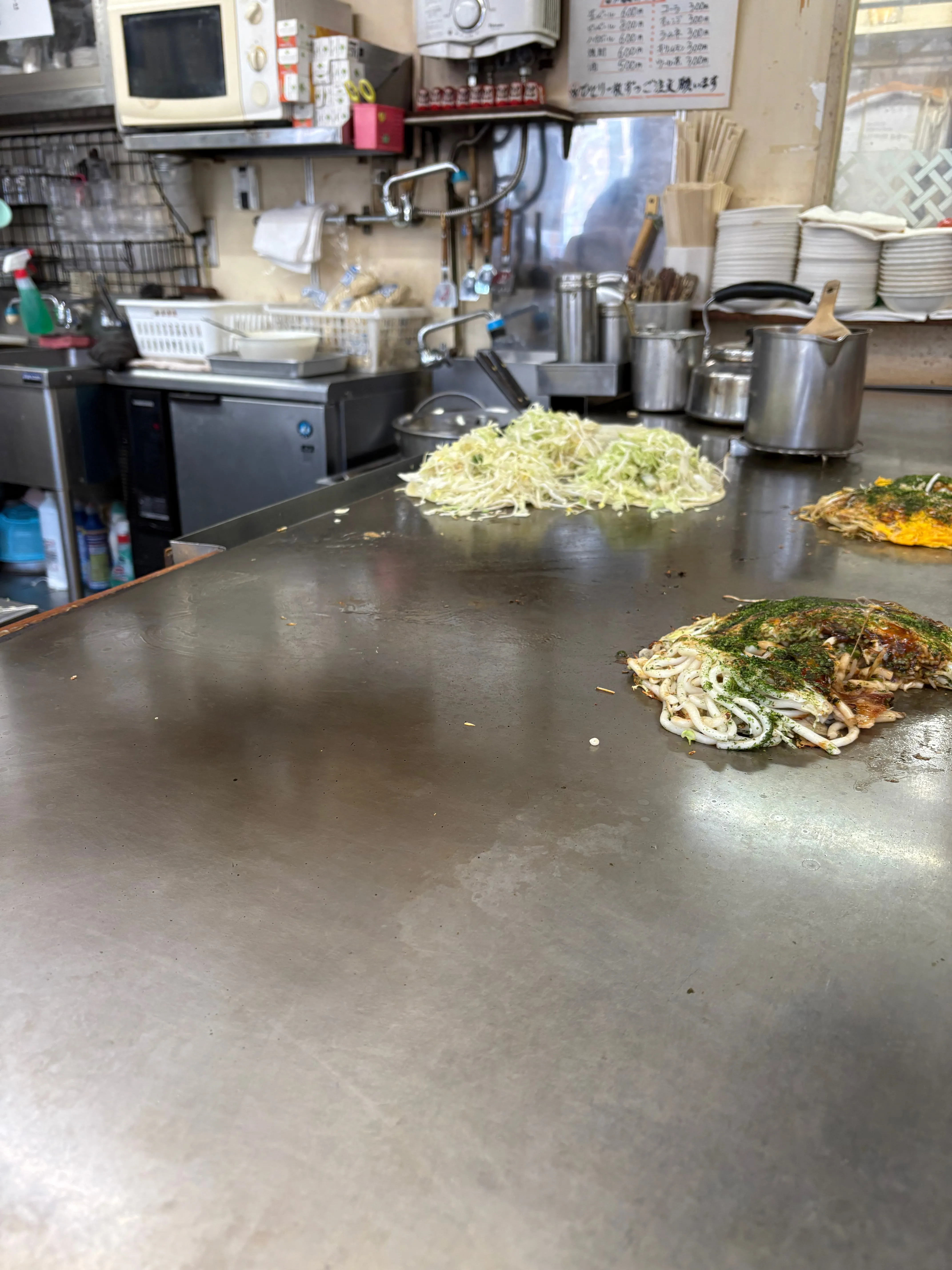 お好み焼きの鉄板。キャベツの山と、麺入りのお好み焼き。